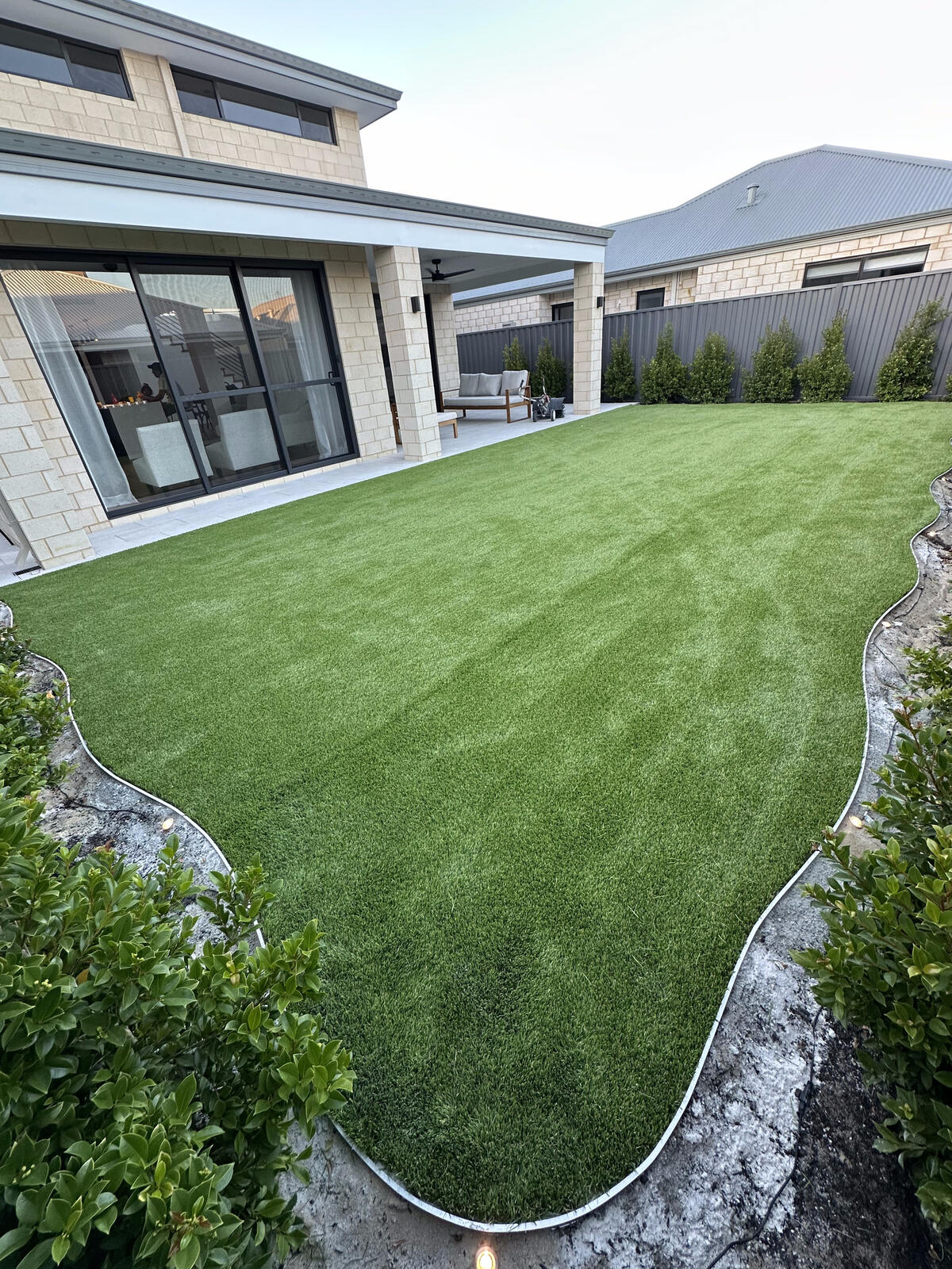 Large backyard artificial turf lawn with hedge screening and paving