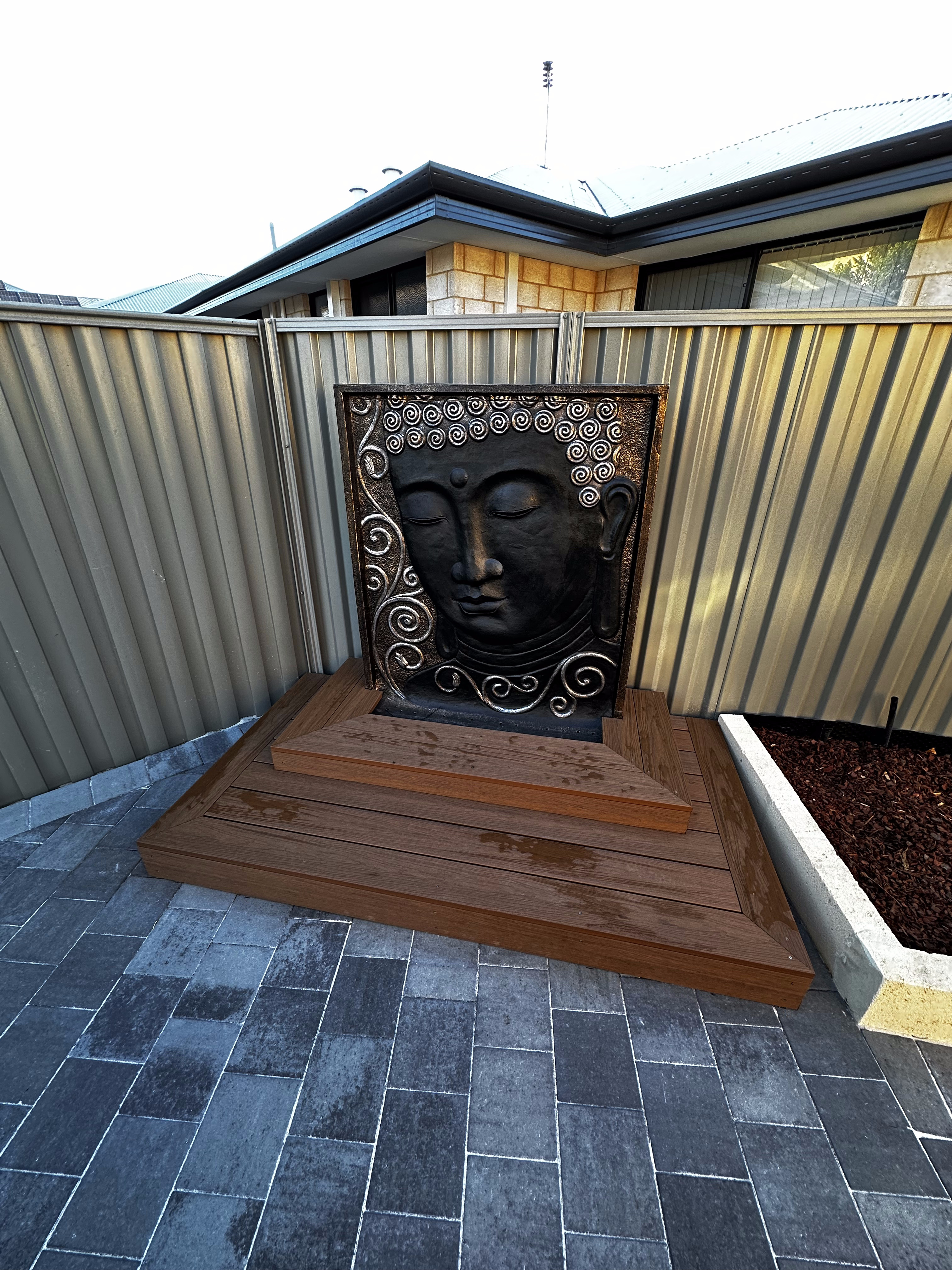 Carved Buddha wall water feature on a timber base