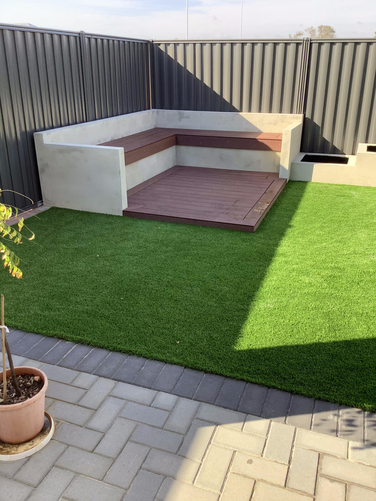 Backyard corner with artificial turf, composite decking and paving