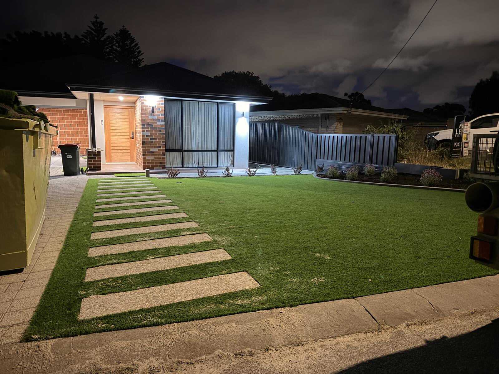 Front yard artificial turf with stepping pavers to the door at night